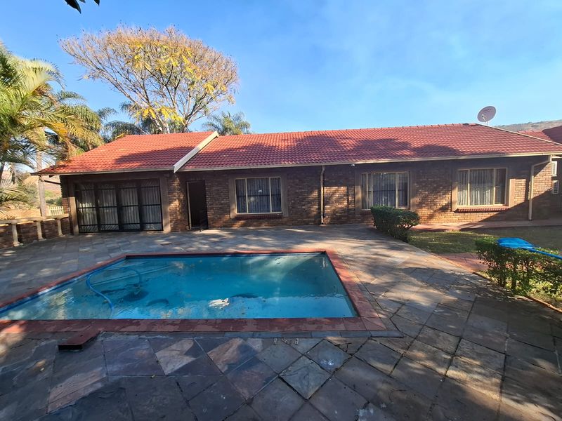 Rear exterior view of a brick house featuring a swimming pool and a paved patio area under a tiled roof.