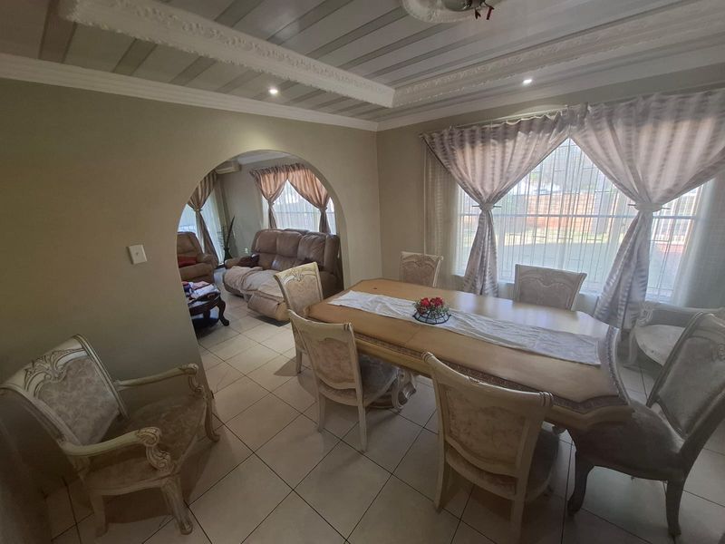 Open plan dining and living area featuring an arched transition, decorative ceiling molding, and tiled flooring throughout.