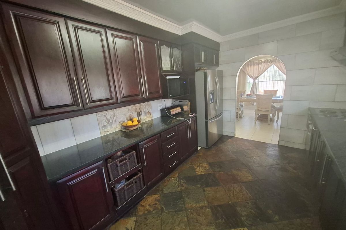 A traditional kitchen featuring dark wood cabinetry, granite countertops, and stone tile flooring, with an arched entryway leading to the dining area.