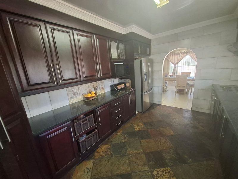 A traditional kitchen featuring dark wood cabinetry, granite countertops, and stone tile flooring, with an arched entryway leading to the dining area.