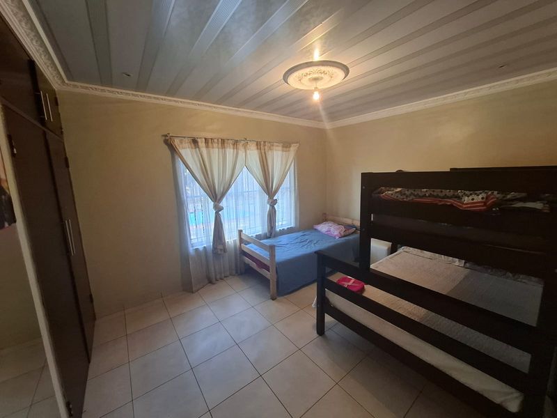 A functional bedroom featuring tiled flooring, built-in cupboards, and decorative ceiling detailing with a central light fixture.