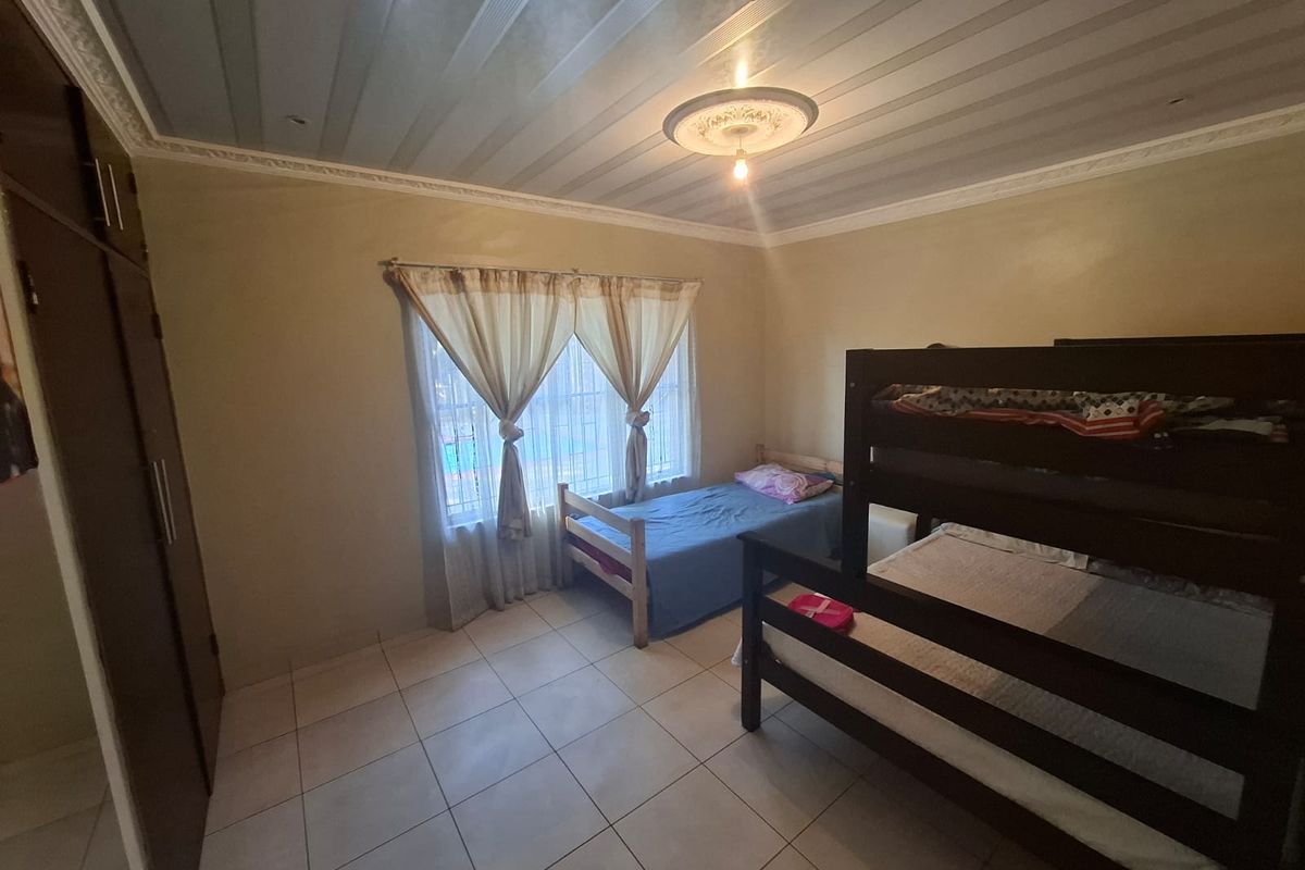 A functional bedroom featuring tiled flooring, built-in cupboards, and decorative ceiling detailing with a central light fixture.