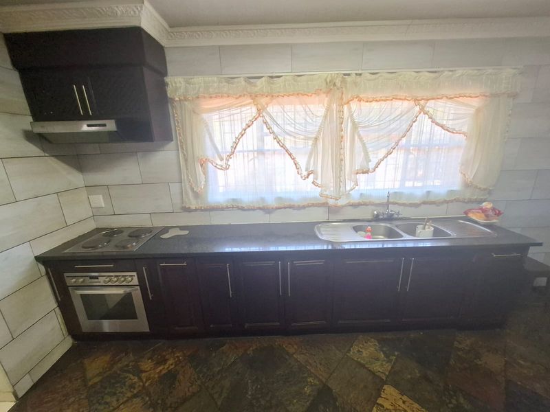 A functional kitchen featuring dark wood cabinetry, a built-in oven with electric hob, extractor fan, and a double sink with tiled splashback.