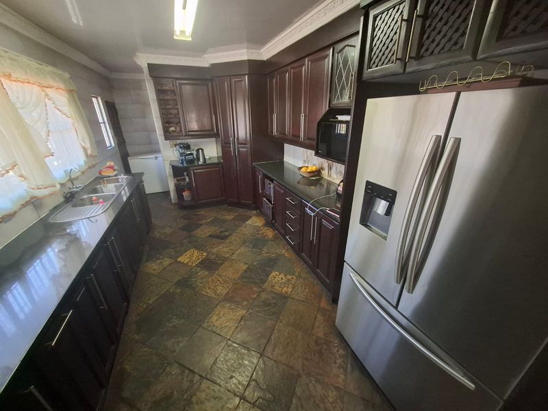 A spacious kitchen featuring dark wood cabinetry, granite countertops, slate tile flooring, and crown molding, offering a traditional aesthetic with ample storage space.