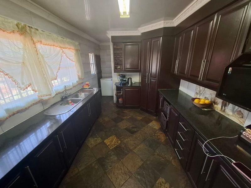 A functional kitchen featuring dark wood cabinetry, granite countertops, double basin sink, and durable slate tile flooring with classic crown molding details.