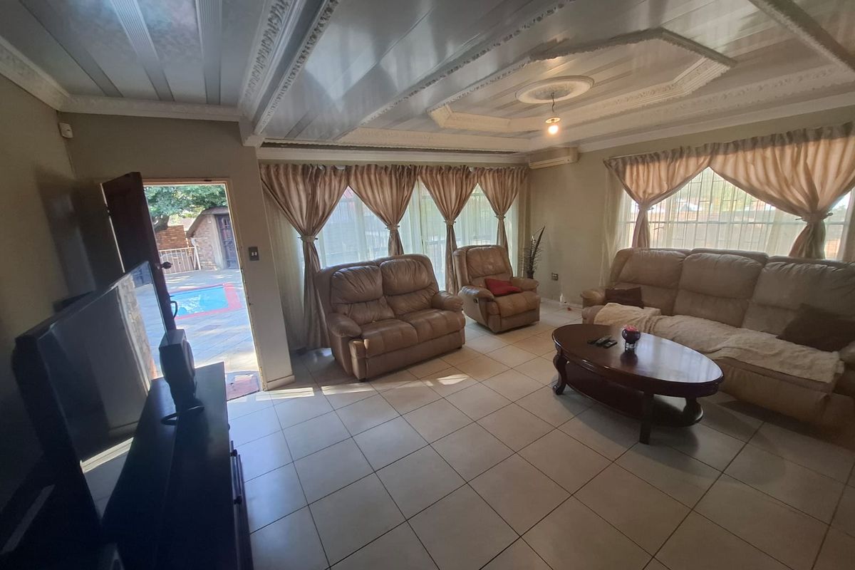 Spacious living room featuring tiled flooring, decorative ceiling molding, and large sliding glass doors providing direct access to the outdoor pool area.