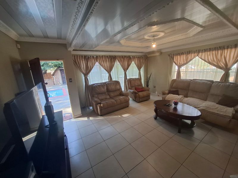 Spacious living room featuring tiled flooring, decorative ceiling molding, and large sliding glass doors providing direct access to the outdoor pool area.