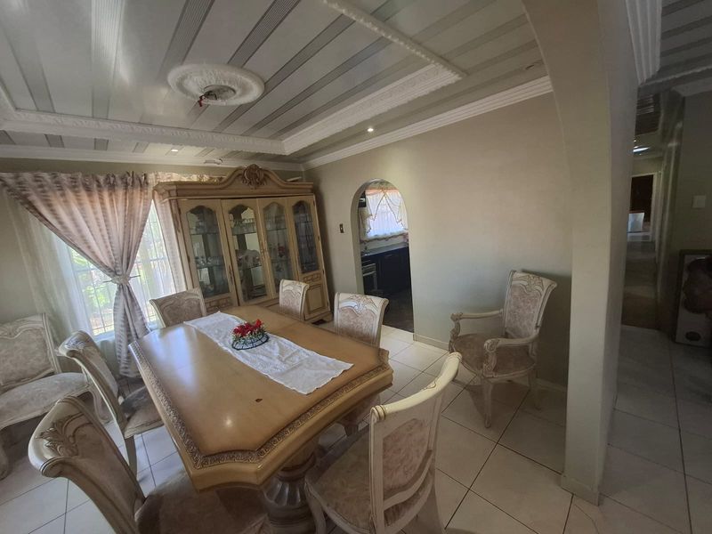 A dining room featuring tiled flooring, decorative ceiling detailing, and an arched entryway leading to the kitchen area.