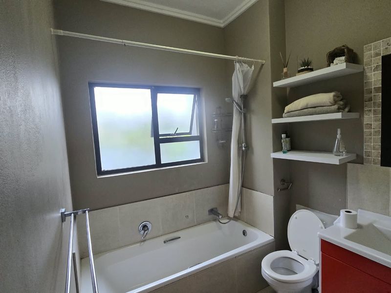 A functional bathroom featuring a built-in bathtub with shower attachment, a vanity basin, and convenient wall-mounted shelving for storage.