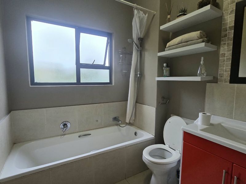 A functional bathroom featuring a built-in bathtub with shower attachment, a vanity unit with integrated basin, and convenient wall-mounted shelving.