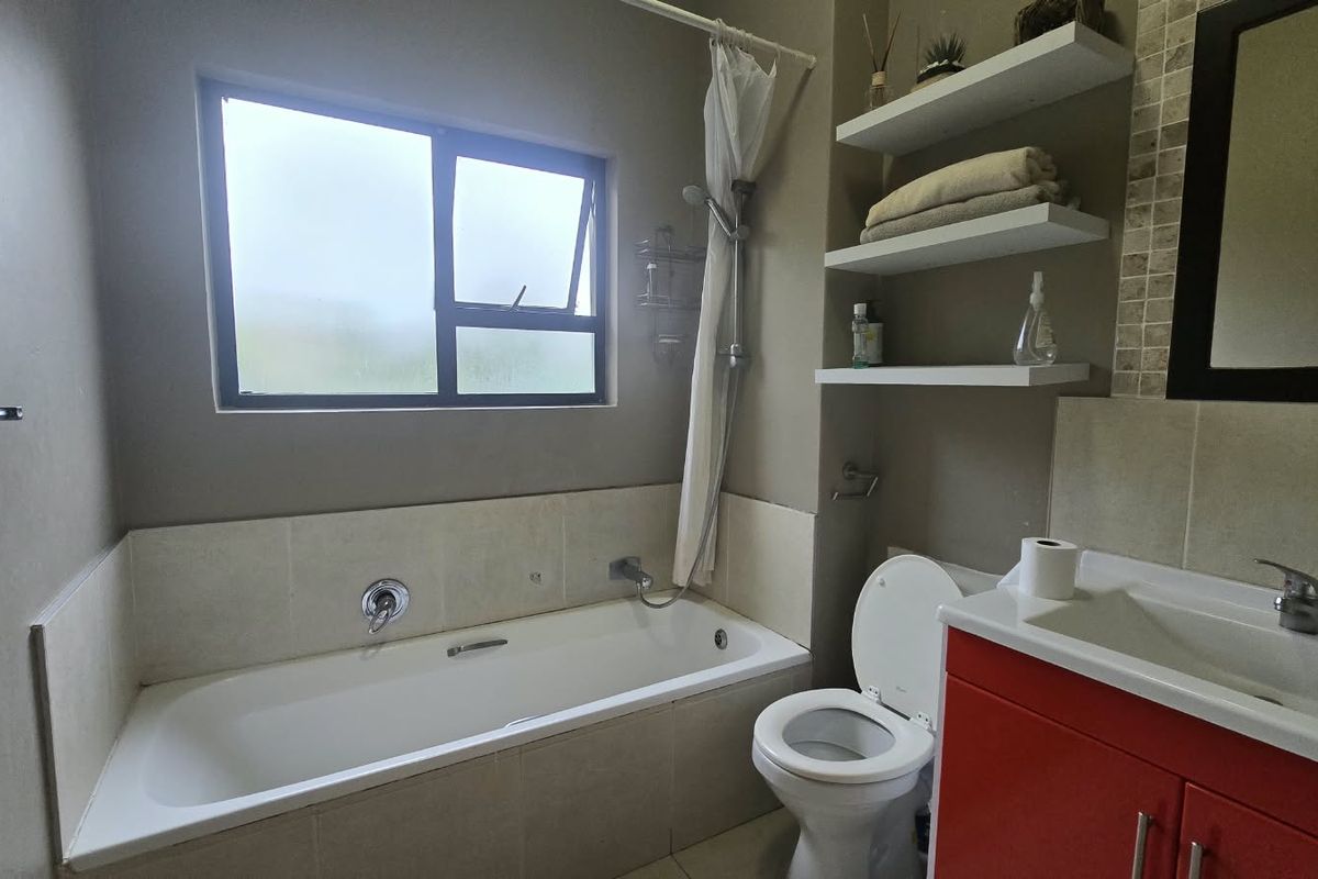 A functional bathroom featuring a built-in bathtub with shower attachment, a vanity unit with integrated basin, and convenient wall-mounted shelving.