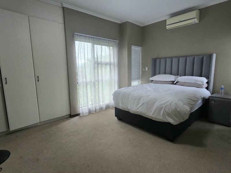 A bedroom featuring built-in cupboards, air conditioning, and carpeted flooring with natural light from the window.