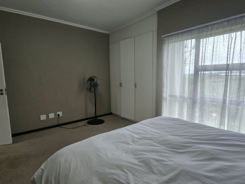 A bedroom featuring neutral wall tones, built-in cupboards, carpeted flooring, and a large window allowing natural light.