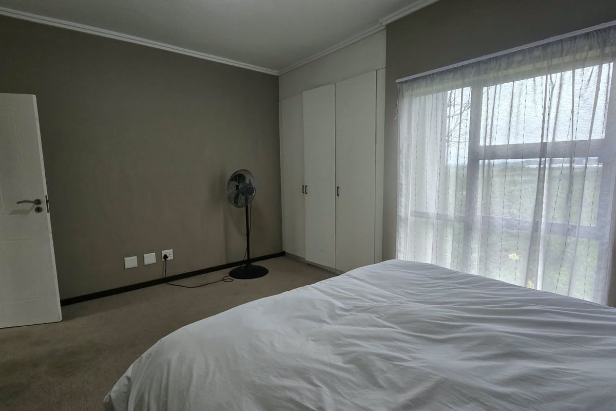 A bedroom featuring neutral wall tones, built-in cupboards, carpeted flooring, and a large window allowing natural light.
