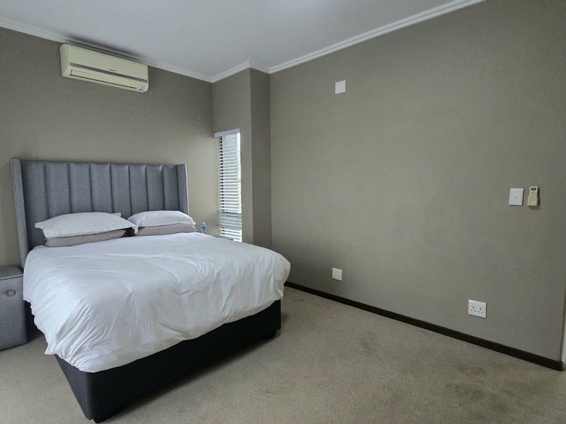A well-maintained bedroom featuring neutral wall tones, carpet flooring, a split-system air conditioner, and direct access to an en-suite bathroom.