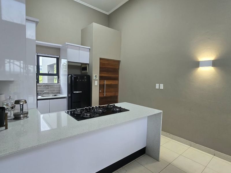 Modern kitchen featuring a central island with a gas hob, quartz countertops, sleek white cabinetry, and tiled flooring in an open-plan layout.