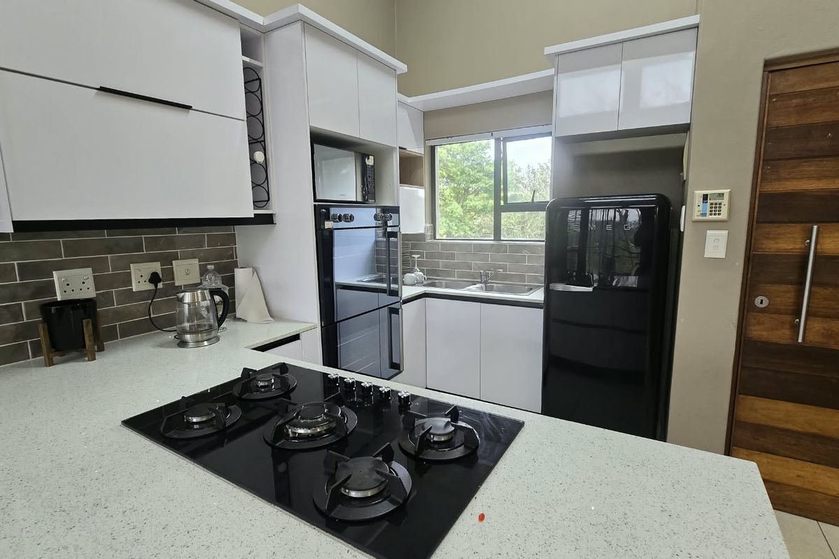Modern kitchen featuring white cabinetry, stone countertops, a gas hob, built-in oven, and a stylish subway tile backsplash with a window view.