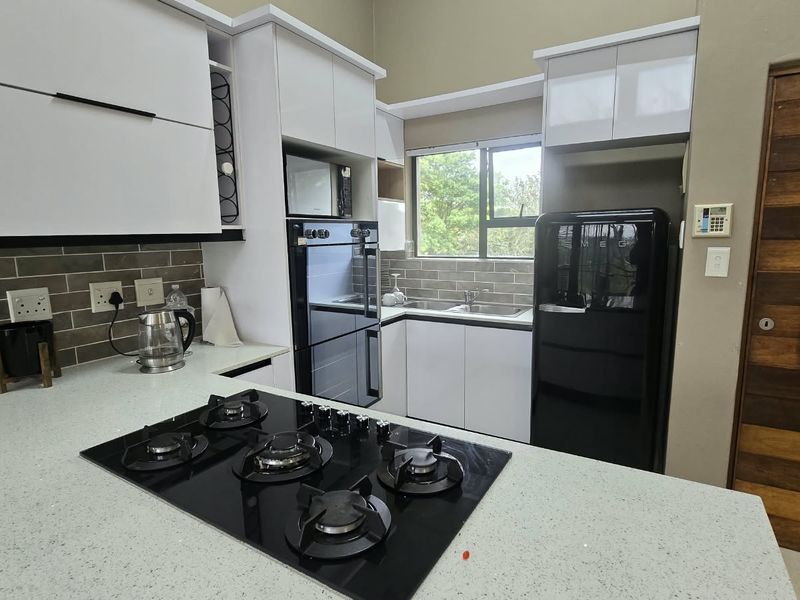 Modern kitchen featuring white cabinetry, stone countertops, a gas hob, built-in oven, and a stylish subway tile backsplash with a window view.