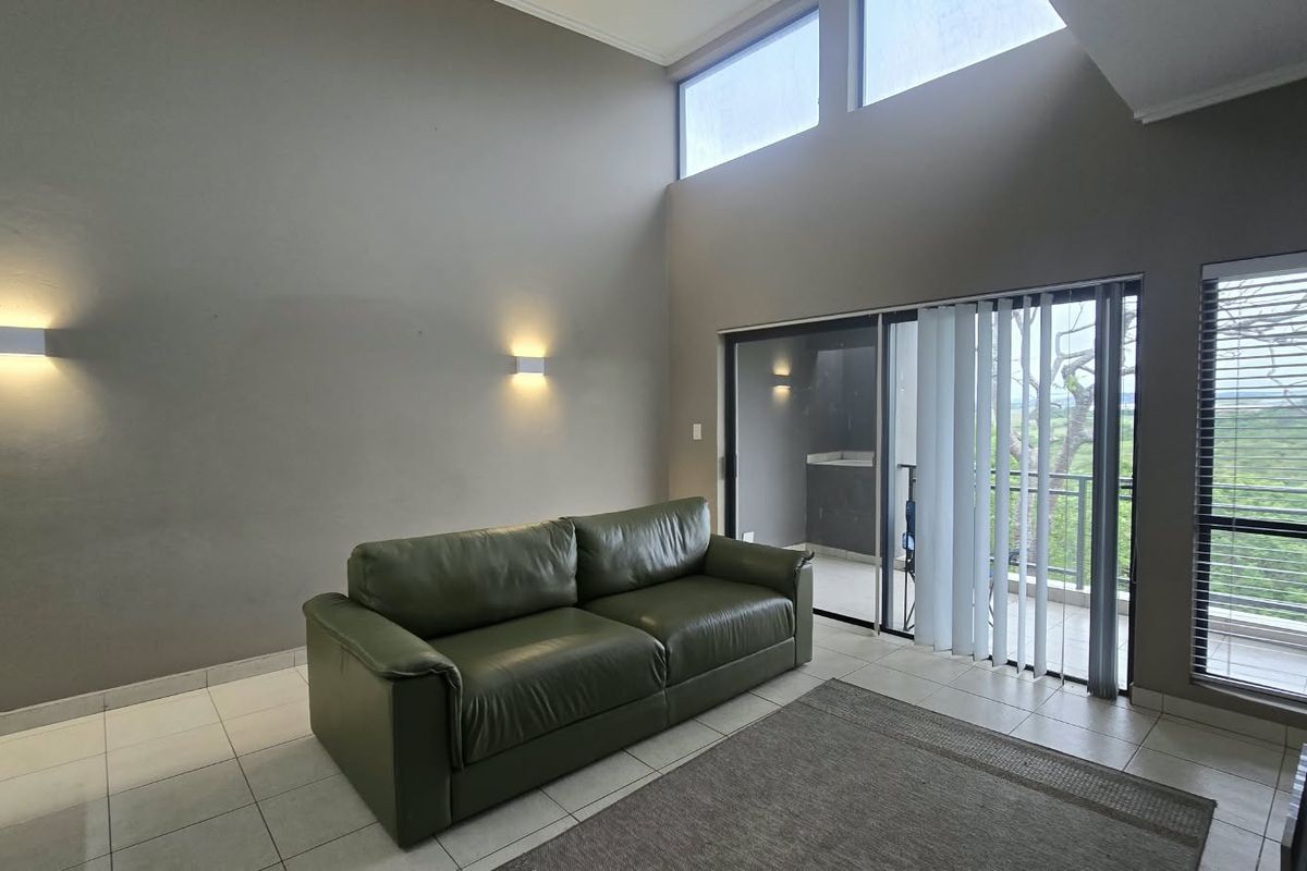 Spacious living room featuring high ceilings, clerestory windows for natural light, tiled flooring, and direct access to a balcony through sliding glass doors.
