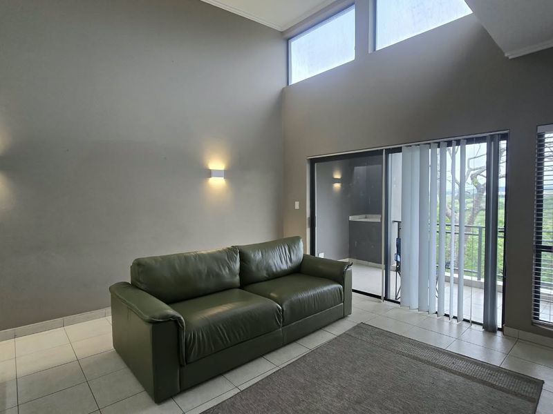 Spacious living room featuring high ceilings, clerestory windows for natural light, tiled flooring, and direct access to a balcony through sliding glass doors.
