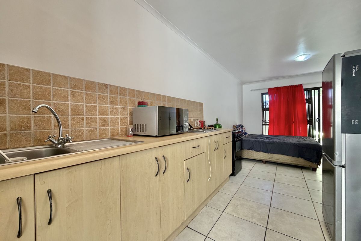 Open-plan studio apartment featuring a functional kitchenette with laminate cabinetry, tiled backsplash, and ceramic flooring, seamlessly integrated with the living and sleeping area.