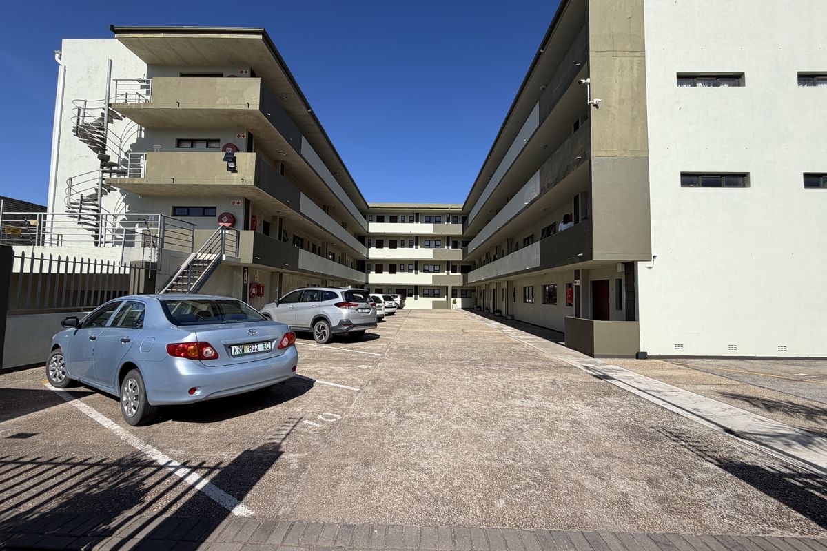 View of the apartment complex courtyard featuring paved parking, external concrete staircases, and multi-level balcony walkways.