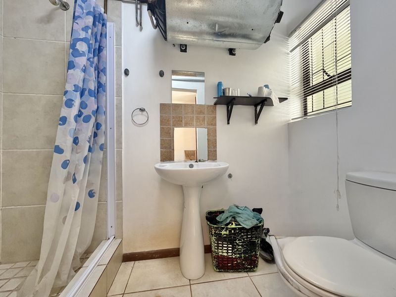 Compact bathroom featuring a pedestal basin, shower enclosure, and toilet. The space requires cosmetic updates and improved finishings to enhance its overall appeal.