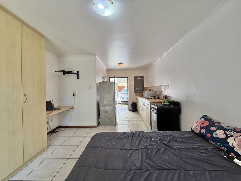 Open-plan studio apartment featuring a compact kitchen area with built-in cabinetry, tiled flooring, and a built-in desk space.