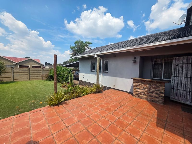 Rear exterior view featuring a tiled patio area with a built-in brick bar counter, overlooking a private garden with precast boundary walling.