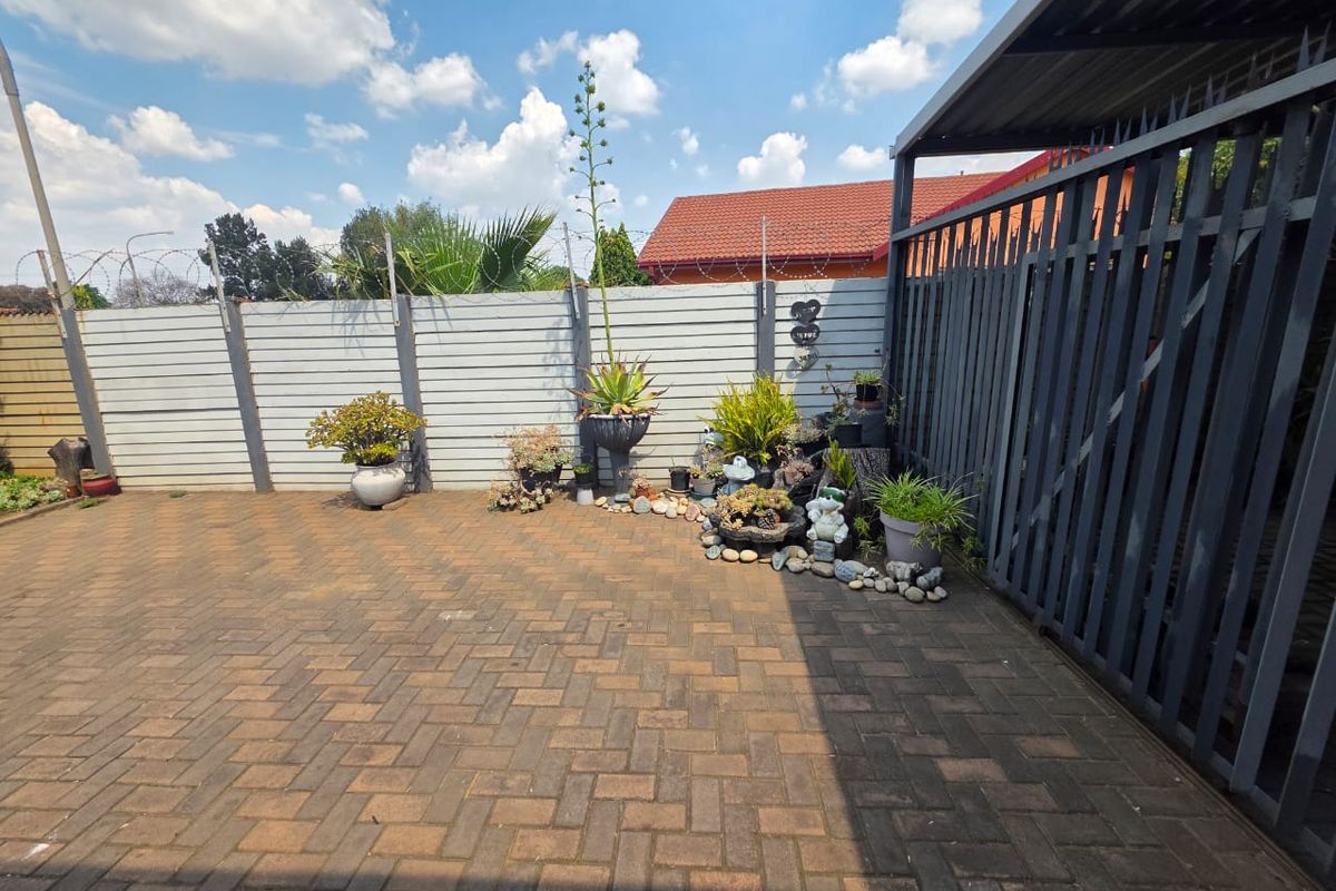 A paved rear courtyard area featuring a precast concrete boundary wall with security razor wire and a metal gate structure.