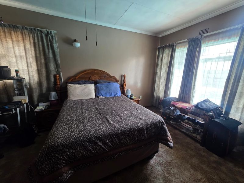 A bedroom featuring large windows with security bars, wall-mounted lighting, and carpeted flooring, offering a functional space with potential for cosmetic updates.