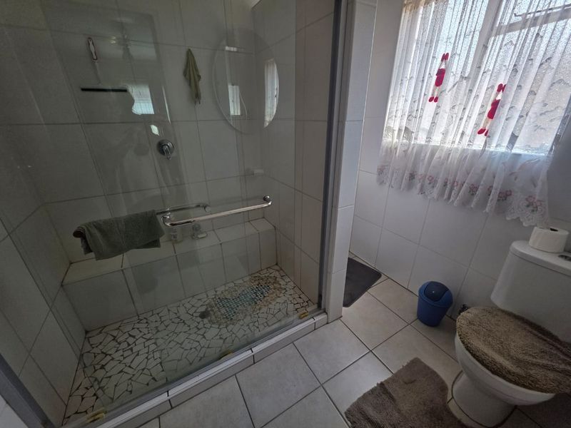 A functional bathroom featuring a glass-enclosed shower with a built-in bench, mosaic tiled shower floor, and standard ceramic wall and floor tiling.