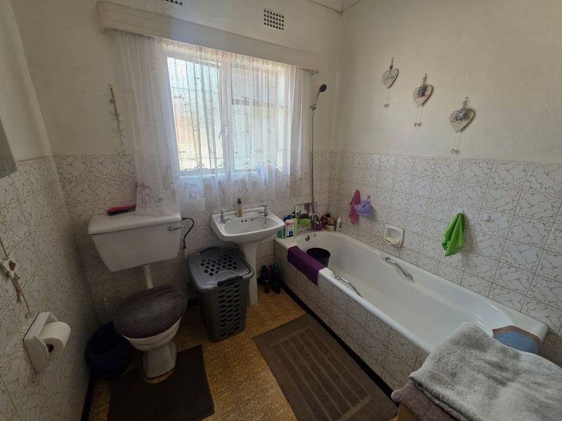A functional bathroom featuring a bathtub with shower attachment, pedestal basin, and toilet, finished with classic ceramic wall tiling.