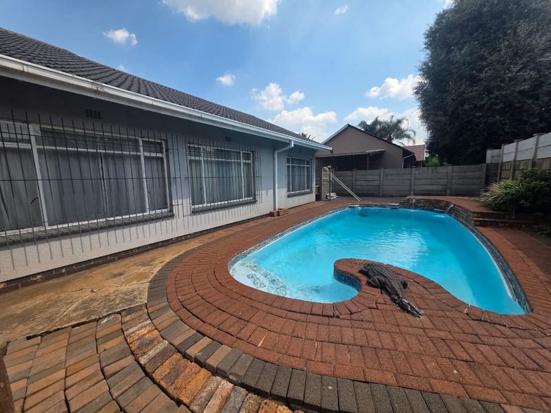 Rear exterior view featuring a swimming pool with brick paving surround, concrete boundary walls, and security bars on the house windows.