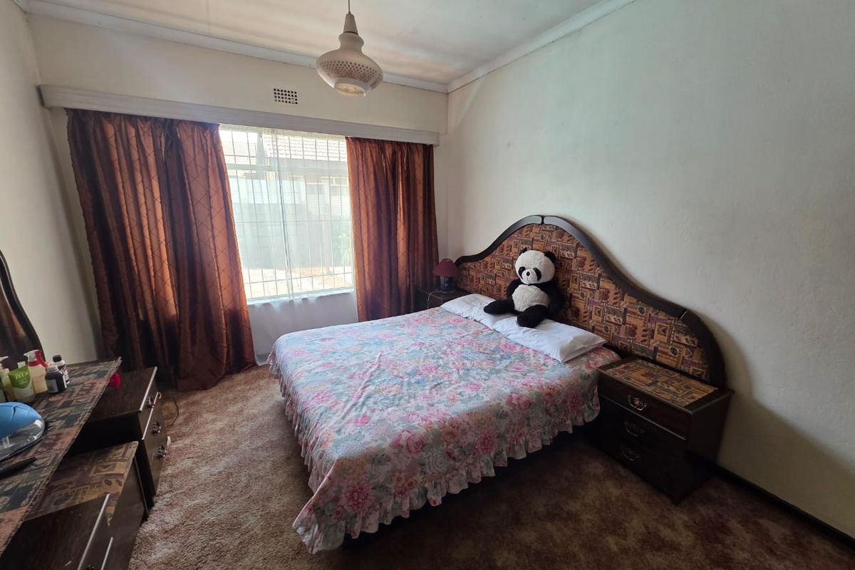 A bedroom featuring carpeted flooring, a large window with curtain rails, and a ceiling light fixture, offering a functional space for renovation.