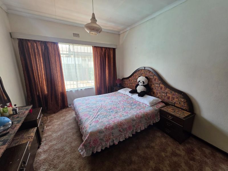 A bedroom featuring carpeted flooring, a large window with curtain rails, and a ceiling light fixture, offering a functional space for renovation.