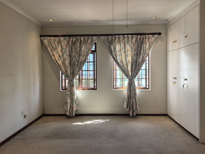 A vacant bedroom featuring built-in cupboards, carpeted flooring, and windows fitted with security bars.