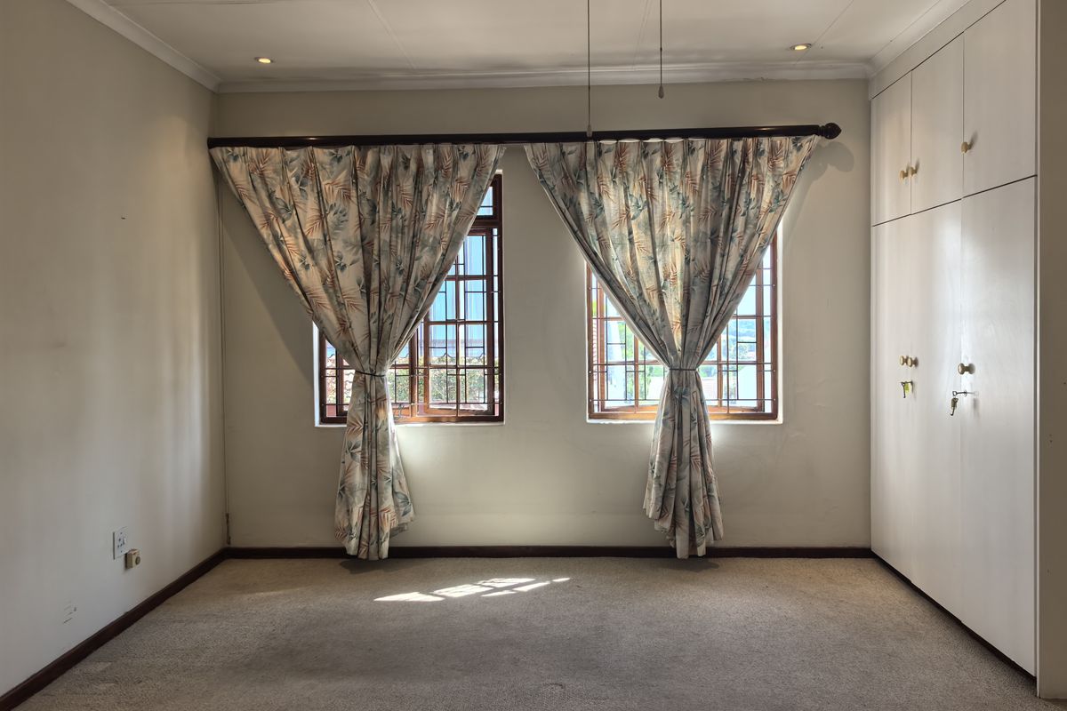 A vacant bedroom featuring built-in cupboards, carpeted flooring, and windows fitted with security bars.