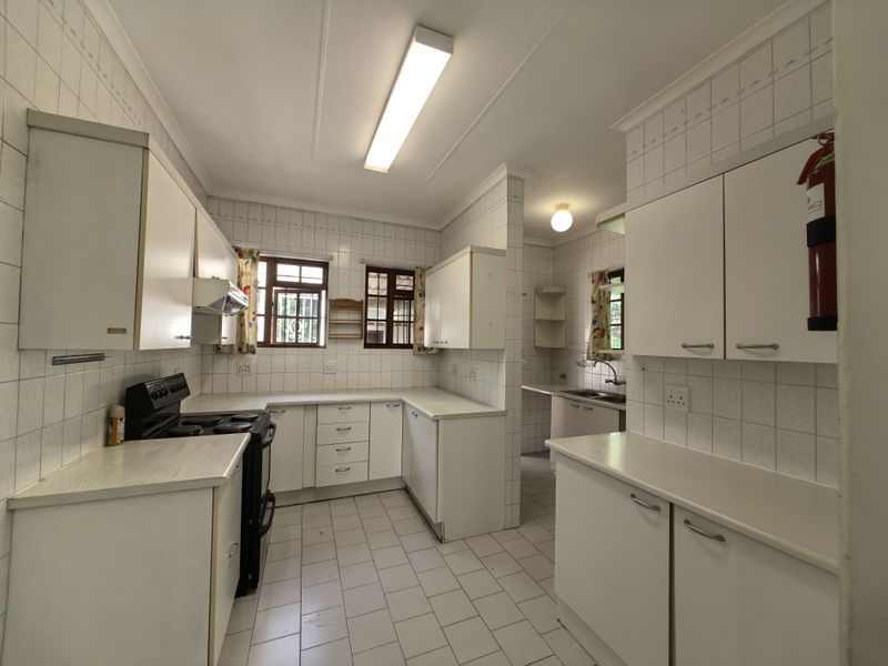 A functional kitchen featuring white built-in cabinetry, tiled splashbacks, tiled flooring, and a separate scullery area with a double sink.