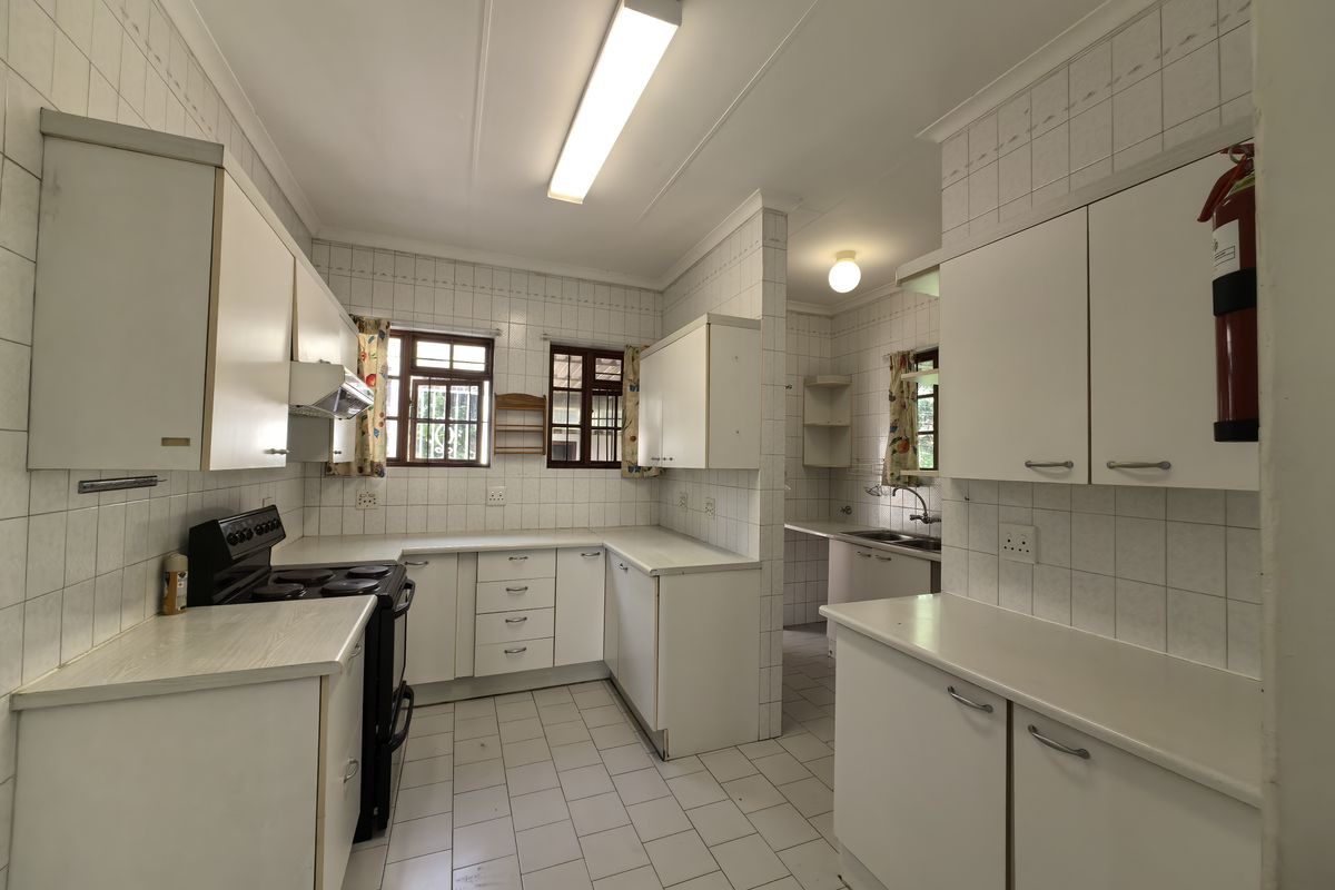 A functional kitchen featuring white built-in cabinetry, tiled splashbacks, tiled flooring, and a separate scullery area with a double sink.
