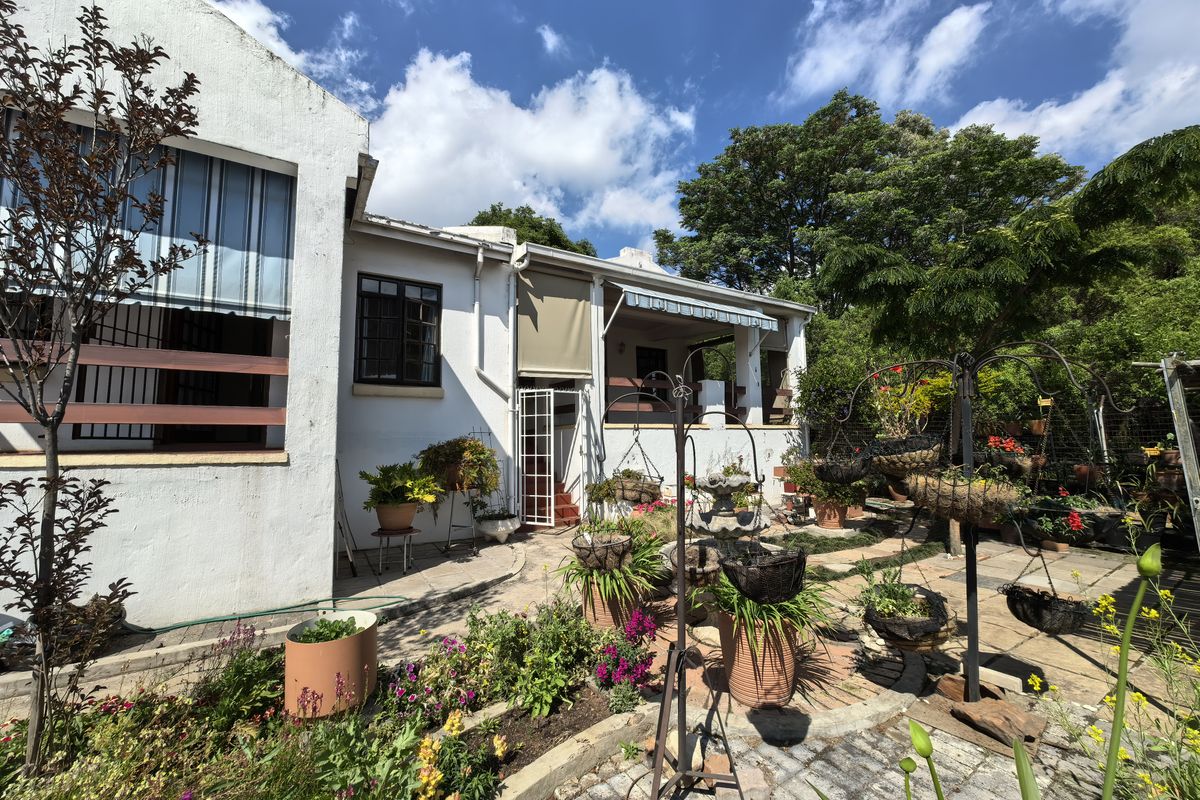 Rear view of the property featuring a paved courtyard, covered patio area with retractable awnings, and established garden beds.