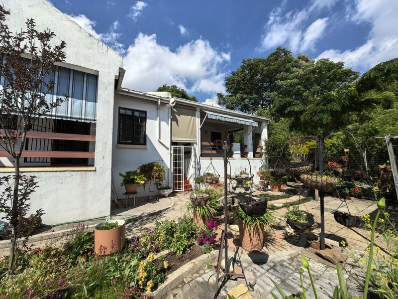 Rear view of the property featuring a paved courtyard, covered patio area with retractable awnings, and established garden beds.