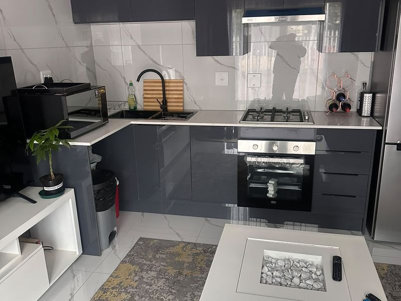 Modern open-plan kitchen featuring high-gloss grey cabinetry, marble-effect wall tiling, integrated oven, gas hob, and sleek stone countertops.