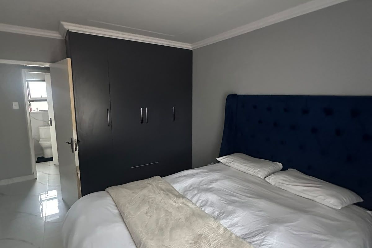 A well-maintained bedroom featuring modern white marble-look floor tiles, a dark built-in wardrobe, and direct access to an en-suite bathroom.