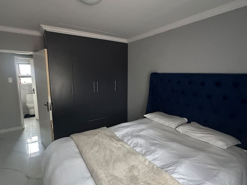 A well-maintained bedroom featuring modern white marble-look floor tiles, a dark built-in wardrobe, and direct access to an en-suite bathroom.