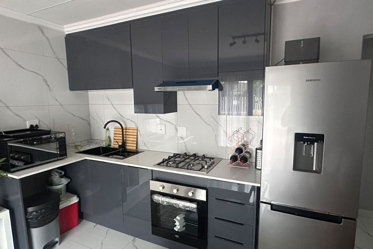 Modern kitchen featuring high-gloss grey cabinetry, marble-look wall tiles, stone countertops, and integrated stainless steel appliances.