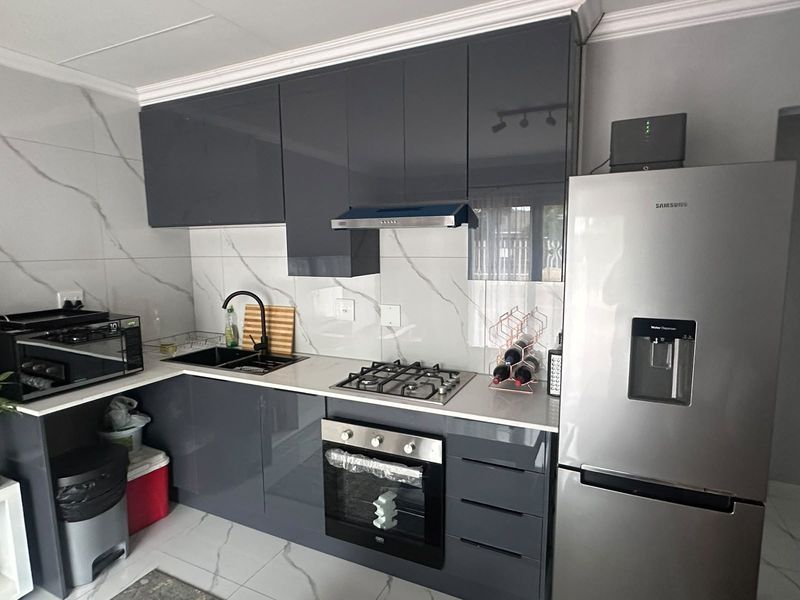 Modern kitchen featuring high-gloss grey cabinetry, marble-look wall tiles, stone countertops, and integrated stainless steel appliances.