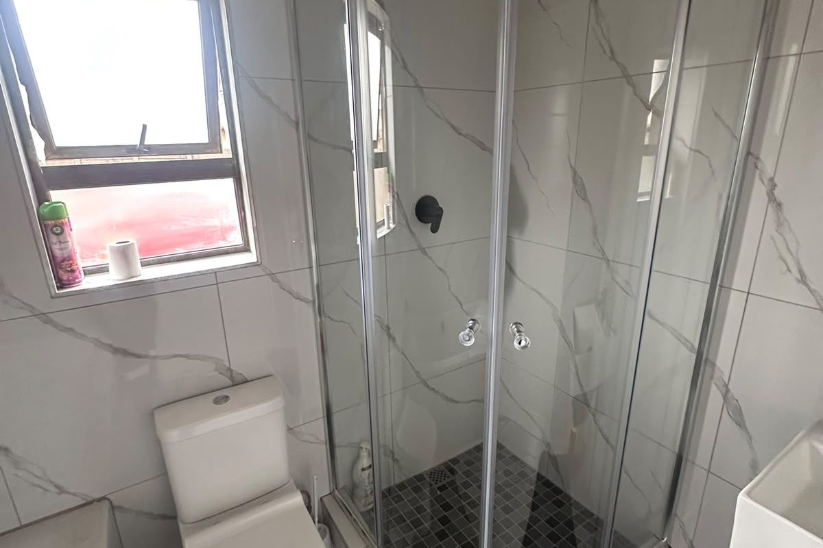 Modern bathroom featuring a corner shower enclosure with a rain shower head, a white toilet, and a wall-mounted basin with marble-look tiling.