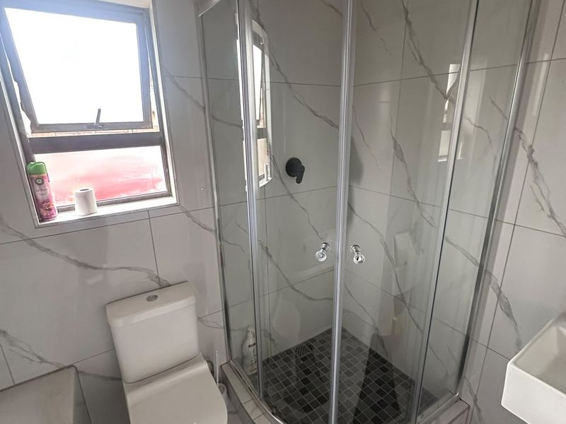 Modern bathroom featuring a corner shower enclosure with a rain shower head, a white toilet, and a wall-mounted basin with marble-look tiling.
