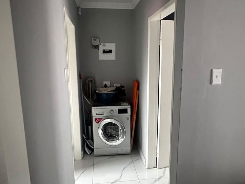 A functional laundry area featuring tiled flooring and a dedicated space for a washing machine, situated within a clean, neutral hallway.